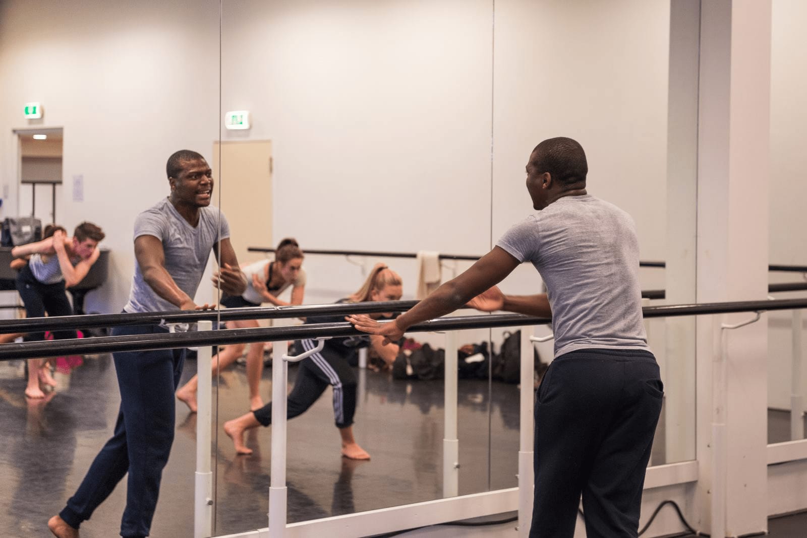 an image of Elvis Sibeko in front of a huge mirror in a gymnasium and teaching people behind him how to dance  