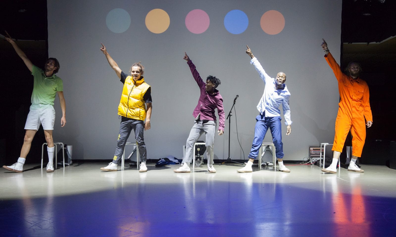 an image of five men standing in a row in a studio and all pointing up